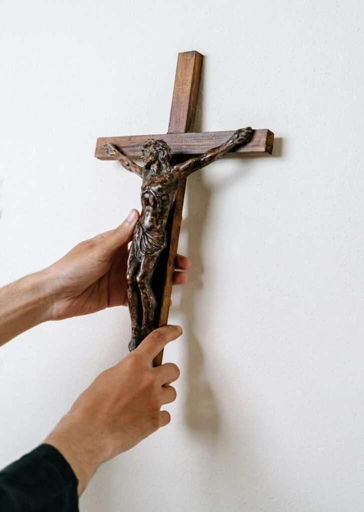 Close-up image of hands placing a wooden crucifix on a white wall emphasizing spirituality.